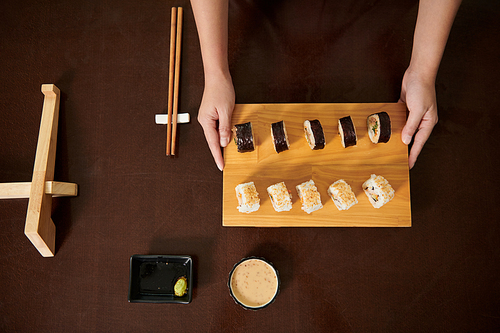 Hands of woman holding bamboo sushi board with sushi, view from above