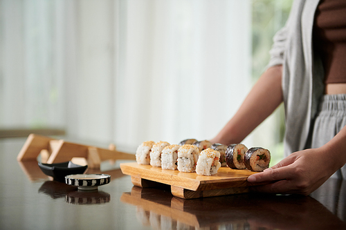 Woman putting homemade sushi and sauce on dinner table