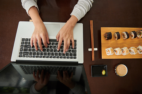 Hands of businesswoman eating sushi when working on laptop at cafe table