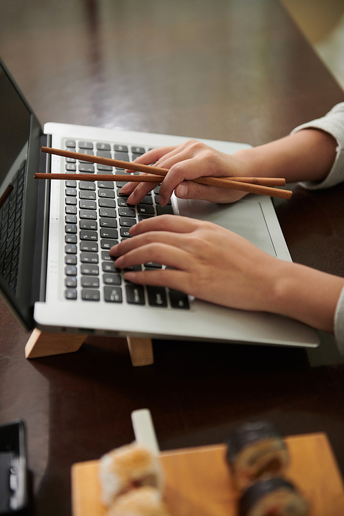 Female entrepreneur with chopsticks in hand working on laptop