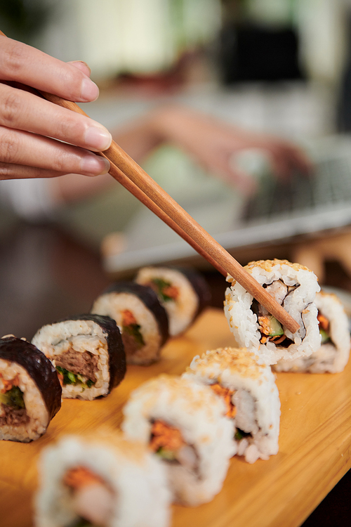 Hand of woman eating delicious homemade sushi with chopsticks