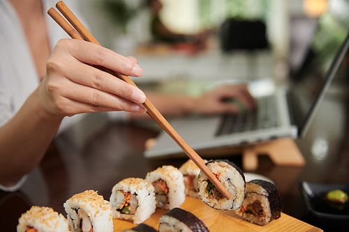 Hands of young woman using chopsticks when eating sushi for dinner