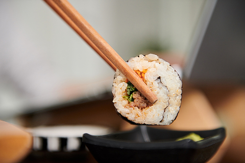 Closeup image of woman dipping sushi in small bowl of soy sauce