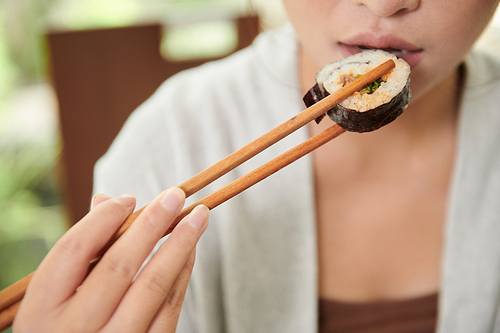 Young woman with chopsticks eating sushi for dinner in cafe