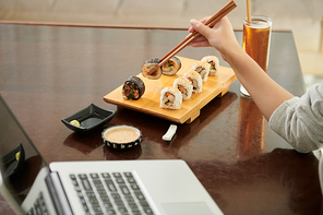 Cropped image of female freelancer eating sushi in cafe when working on laptop