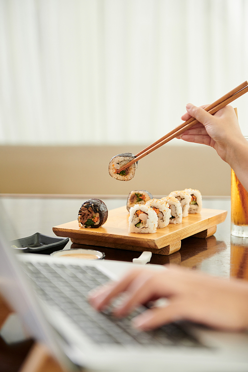 Young woman working on laptop and eating sushi when working on laptop at home
