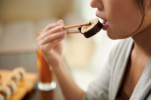 Young woman eating delicious sushi in restaurant