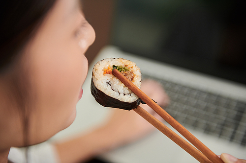 Young woman eating tasty sushi and working on laptop in cafe