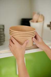 Hands of woman putting disposable bowls on shelf in kitchen cabinet