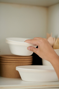 Closeup image of woman taking disposable bowls out of kitchen cabinet