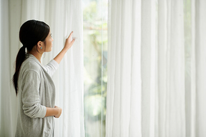 Young woman opening curtains in the morning