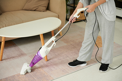 Housewife in loungewear vacuum cleaning floor in apartment