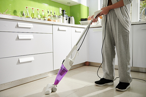 Woman cleaning kitchen floor with steam mop after cooking