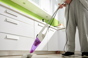 Cropped image of woman in homewear vacuum cleaning floor in kitchen