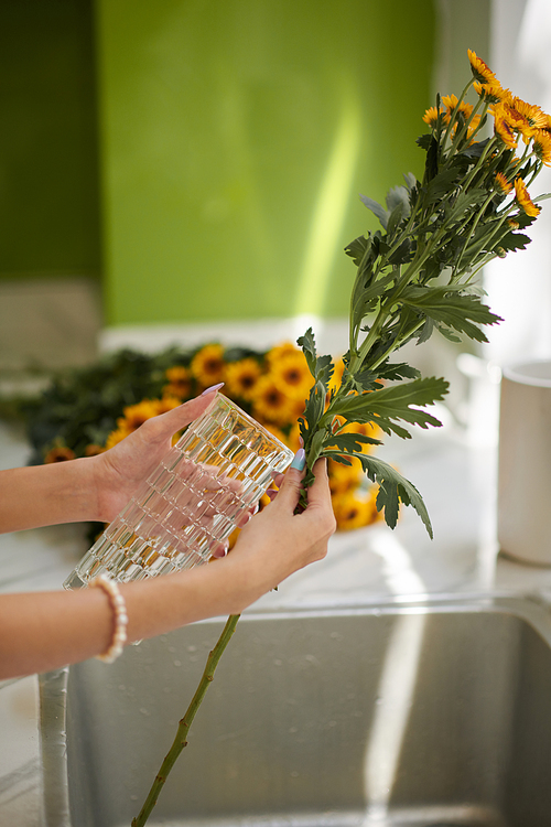 Woman putting flowers in glass vase over kitchen sink
