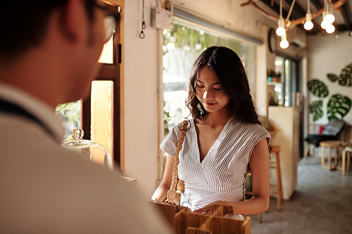 Smiling young Asian woman making order in coffeeshop via tablet computer