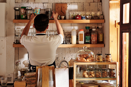 Coffeeshop barista taking jars with black tea from shelf to make drink for customer