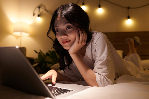 Asian teenage girl relaxing on bed and browsing the internet late at night