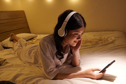 Smiling young Asian woman listening to music and checking posts on social media