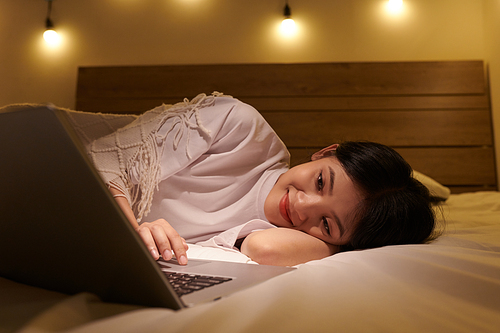Smiling girl resting on bed and watching romantic comedy movie on laptop