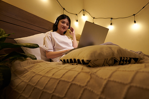 Cheerful teenage girl wearing headphones when watching webinar or educational video on laptop