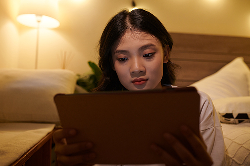 Vietnamese teenage girl reading article on tablet computer at home