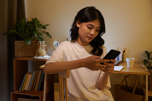 Asian young woman texting friends late at night after finishing doing homework