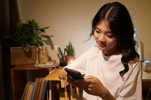 Cheerful teenage girl in pajama texting friends late at night