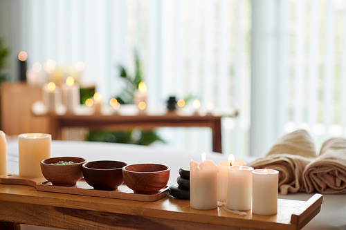 Burning candles and small wooden bowls with various herbs on table in spa salon