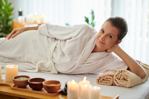 Smiling woman in bathrobe relaxing on bed in spa salon after getting massage