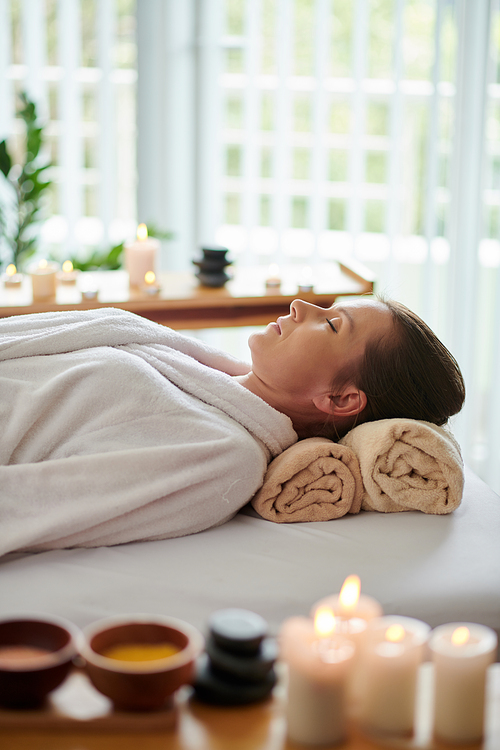 Woman in bathrobe resting on bed in beauty salon after getting relaxing spa procedure