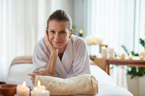 Smiling middle-aged woman lying in bed in spa salon after relaxing massage