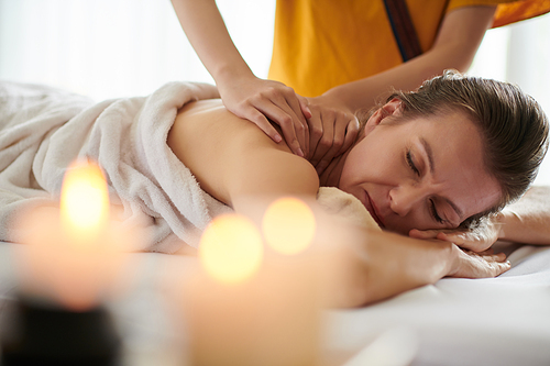 Mature woman getting relaxing shoulder massage in spa salon