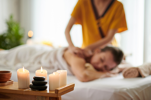 Burning candles in spa salon and woman getting back massage in background