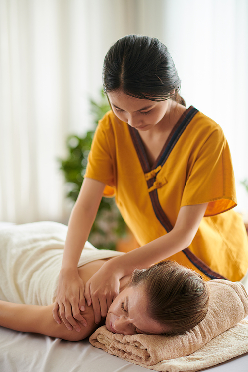 Masseuse massaging back of mature woman in spa salon