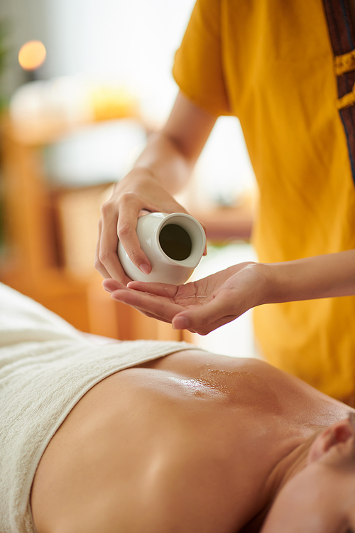 Hands of masseuse applying massage oil on back of woman