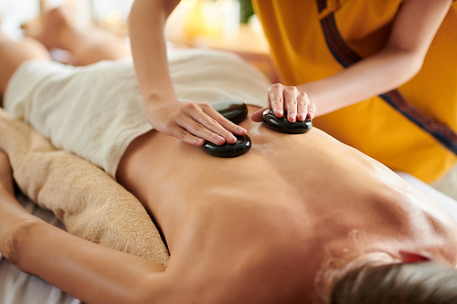 Masseuse putting warm basalt stones on back of woman