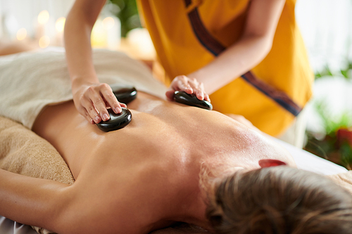 Masseuse putting warm basalt stones on back of female client