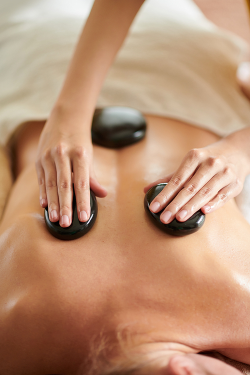 Cropped image of masseuse placing hot round stones on back of woman