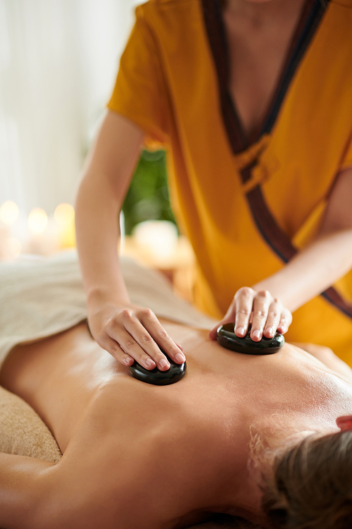 Cropped image of masseuse giving relaxing stone massage to female client