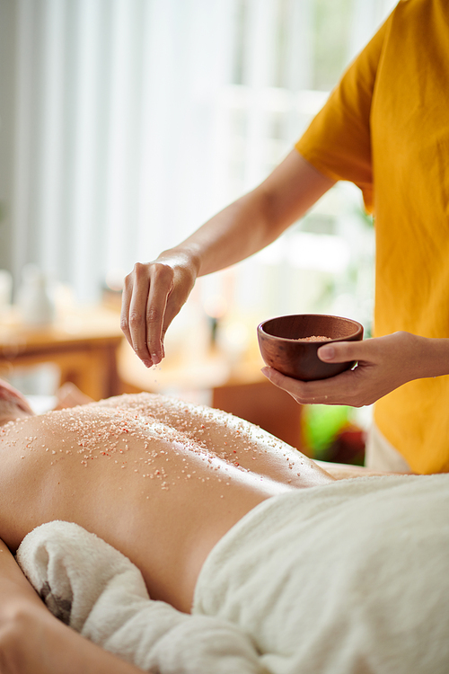 Cropped image of masseuse pinching salt scrub on back of woman