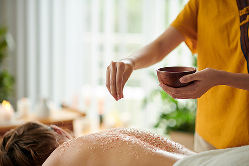 Esthetician applying salt body scrub on back of woman