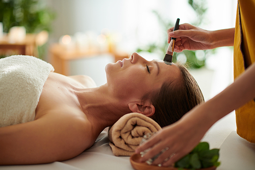 Mature woman getting spa procedure including clay mask in beauty salon