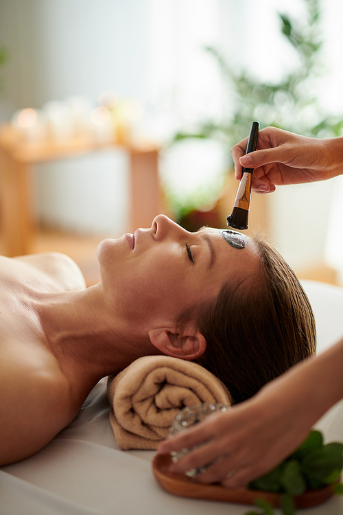 Esthetician applying clay mask on face of mature female client