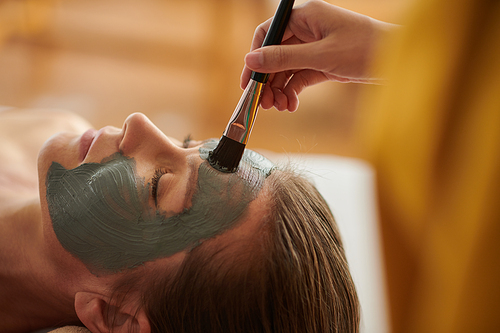 Cropped image of beautician applying purifying clay face mask with brush