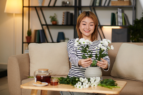 Smiling Asian young woman making flower arrangement with chrysanthemum flowers to decorate house