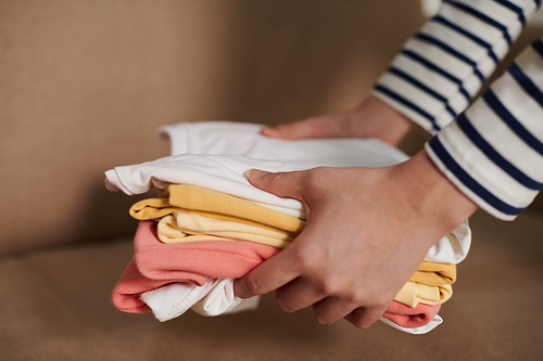 Hands of woman putting folded tidy t-shirts on sofa