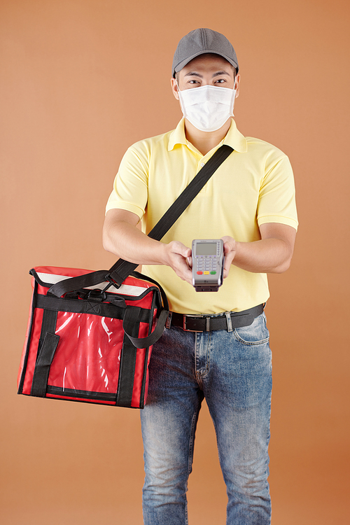 Portrait of courier in medical mask carrying insulated bag and credit card reader