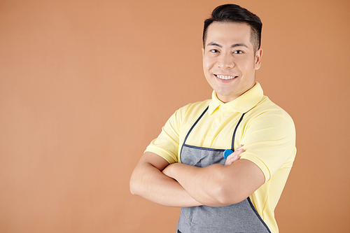 Portrait of happy smiling coffeeshop barista in apron standing with arms crossed and looking at camera