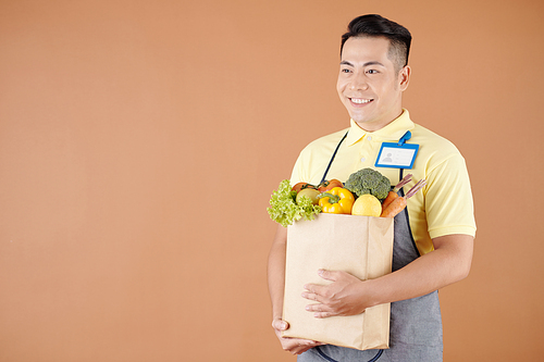 Happy Asian dark store worker carrying bag of fresh products collected for delivery to customer